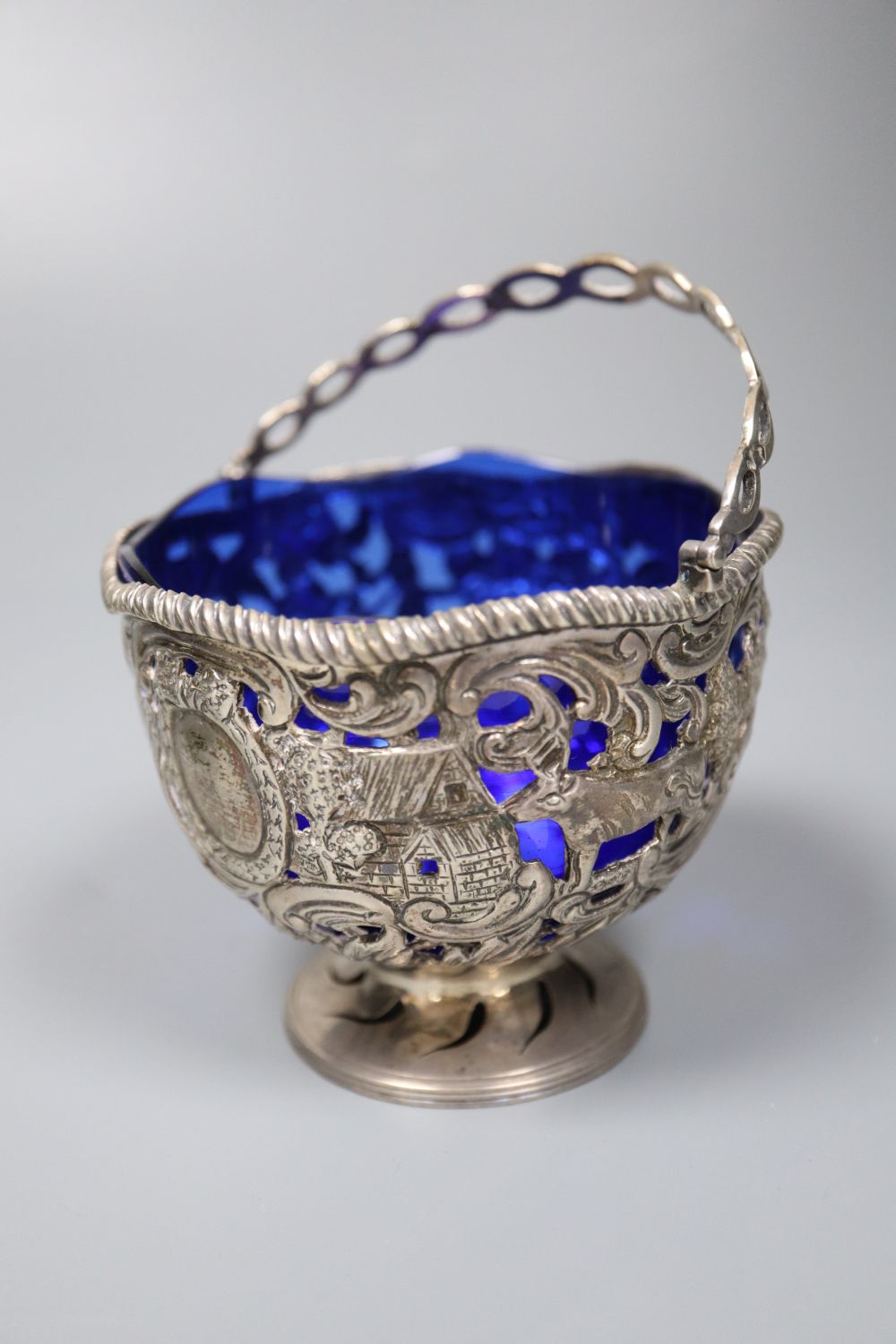 An Edwardian silver sugar basket, George V silver bon-bon dish, silver mounted match strike and a mug salt and spoon (4)